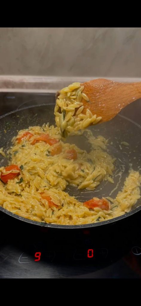 Паста орзо з шматочками форелі, томатами чері та шпинатом у сковороді